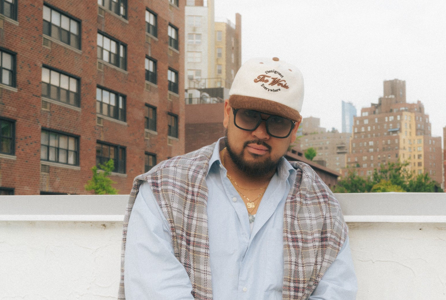 Man wearing a cap and sunglasses on a rooftop with cityscape in the background